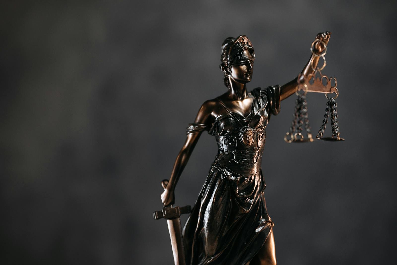 Detailed bronze Lady Justice statue with scales and sword against a dark background, symbolizing law and justice.  